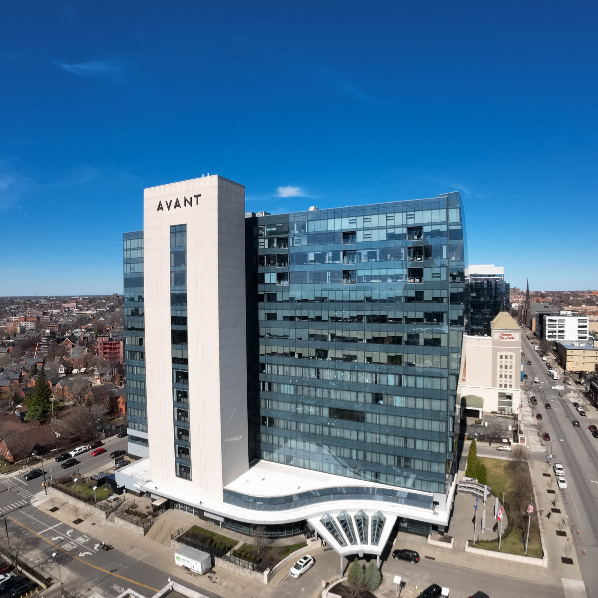 Aerial view of a modern office building labeled 'AVANT', showcasing its glass facade and urban surroundings under a clear blue sky.